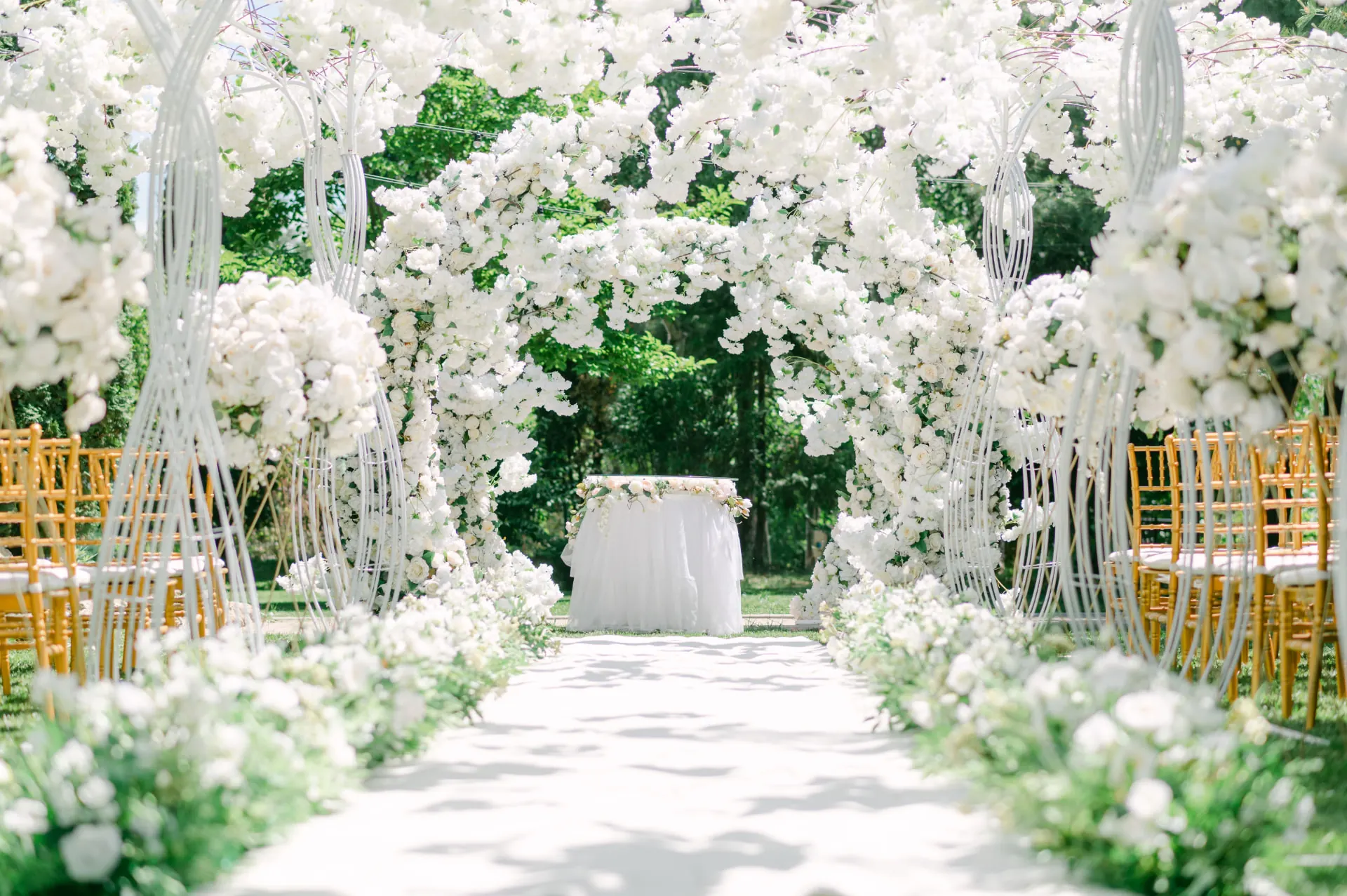 Elegant white floral arch framing an outdoor ceremony aisle